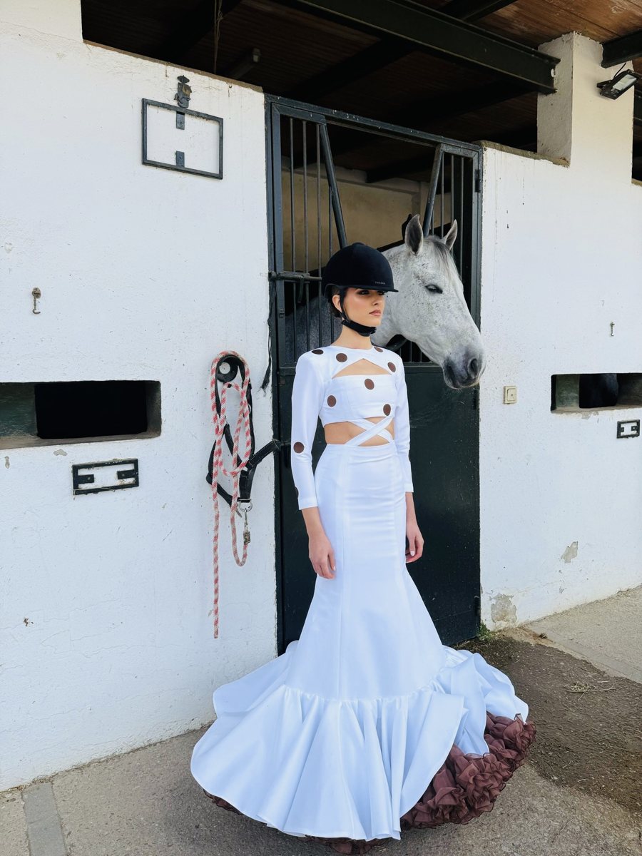Traje de flamenca blanco con lunares marrones junto a un caballo tordo