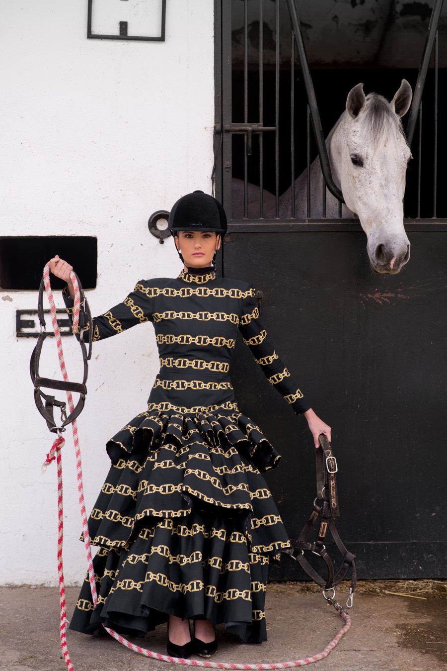 Modelo con traje de volantes estampado de cadenas junto a un caballo en las cuadras