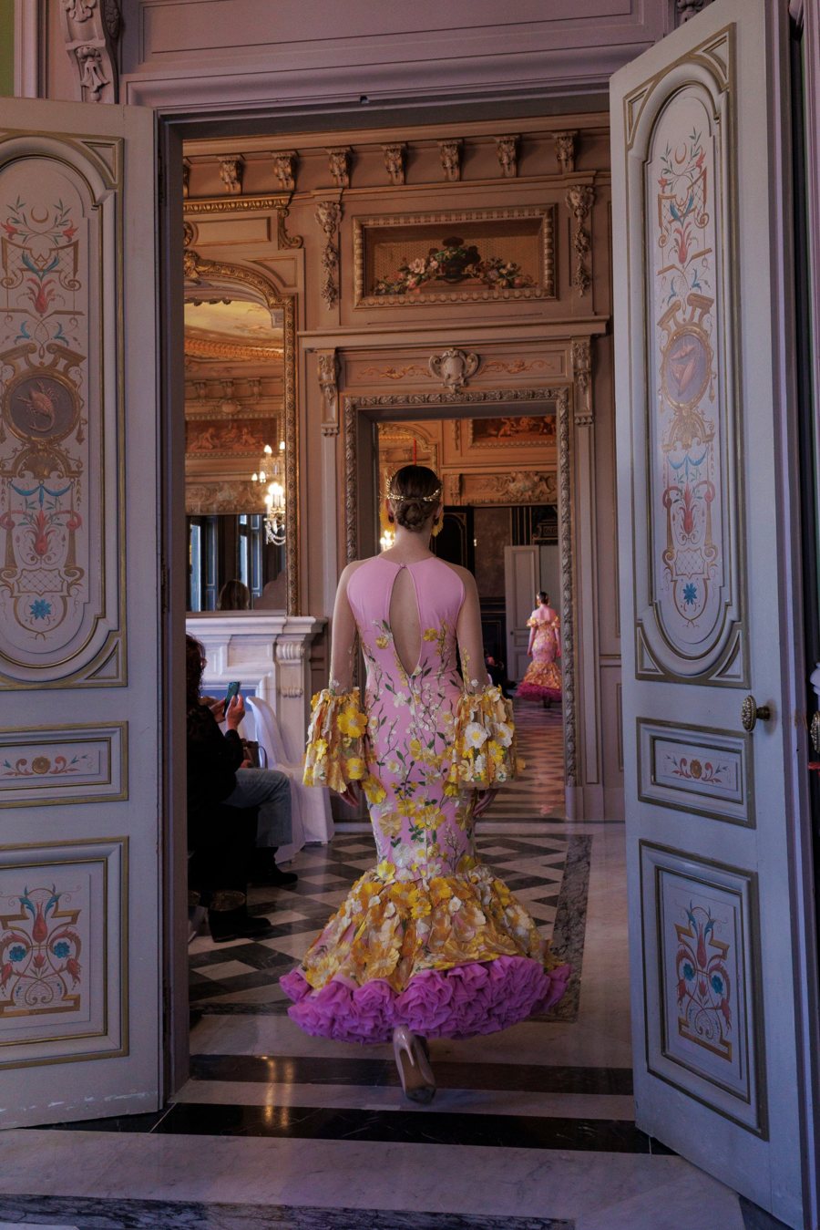 Traje de flamenca rosa con flores amarillas cruzando las puertas pintadas del Palacio